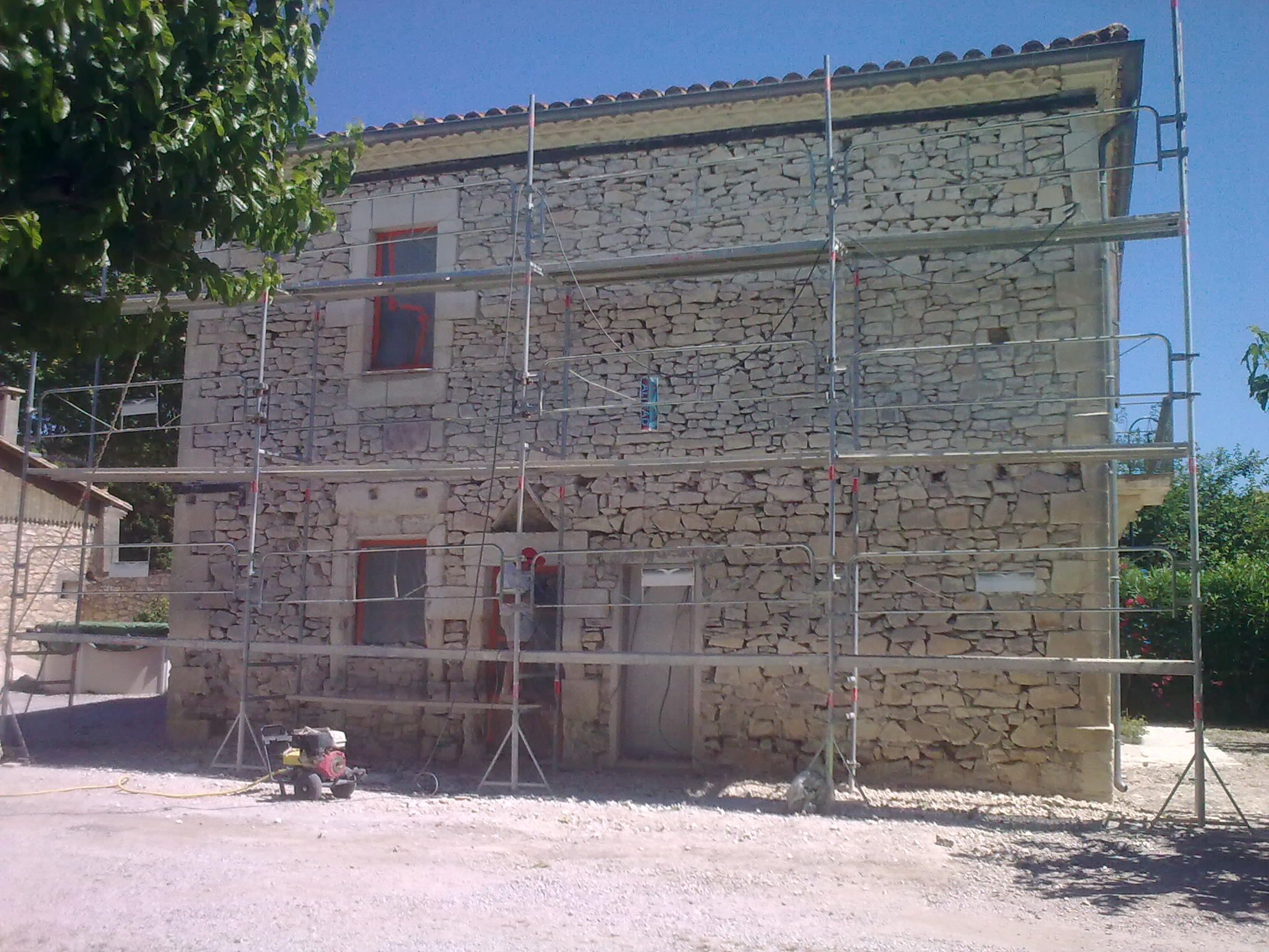 Restauration de la façade d'un mas dans l'Hérault, décroutage des pierres depuis échafaudage.